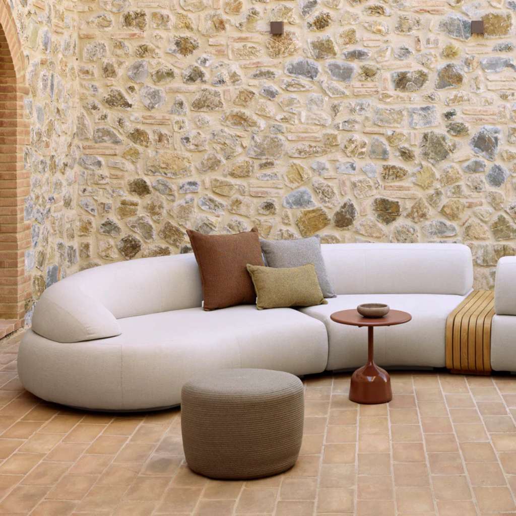 Cane-line curved outdoor sofa with ottoman and side table on patio.