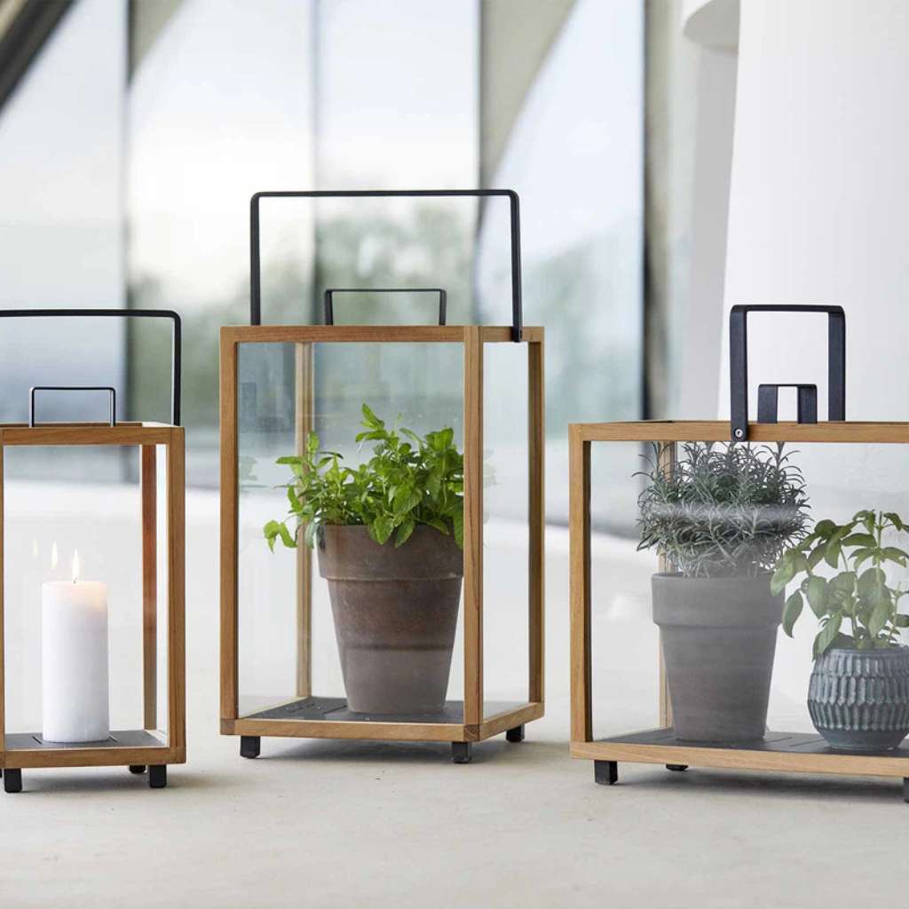 Cane-line teak and glass lantern planters with potted greenery.