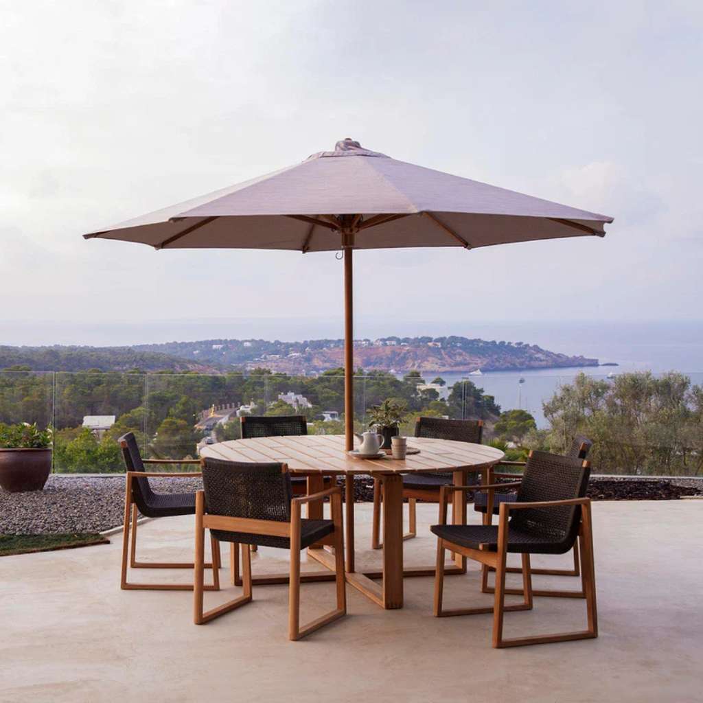 Cane-line teak dining set with woven chairs and parasol on terrace.
