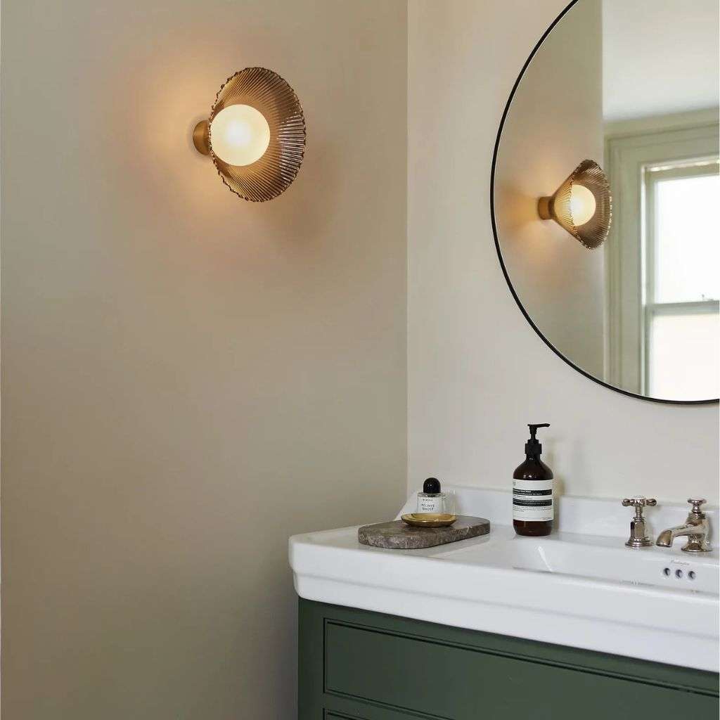 Heathfield ribbed glass wall light beside a round mirror in a refined bathroom