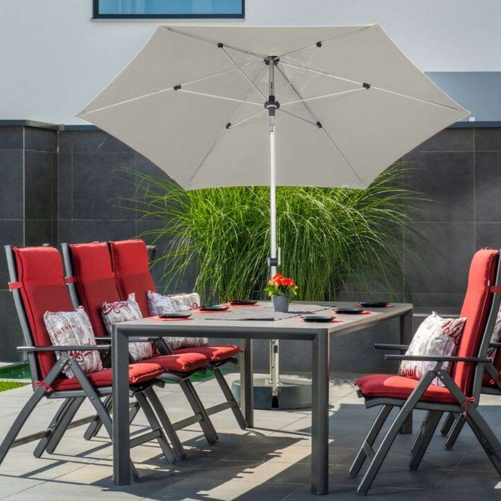 Outdoor dining setup with red cushions under a large umbrella, featuring Kler furniture.