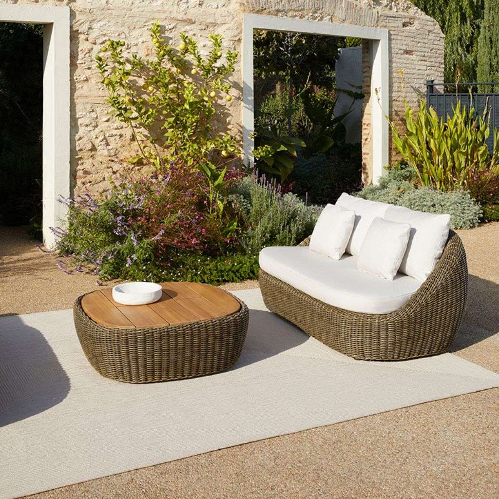 Point outdoor wicker seating set with white cushions surrounded by lush greenery.