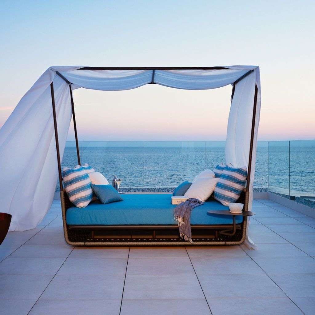 Roberti Rattan outdoor canopy daybed by the ocean at sunset.