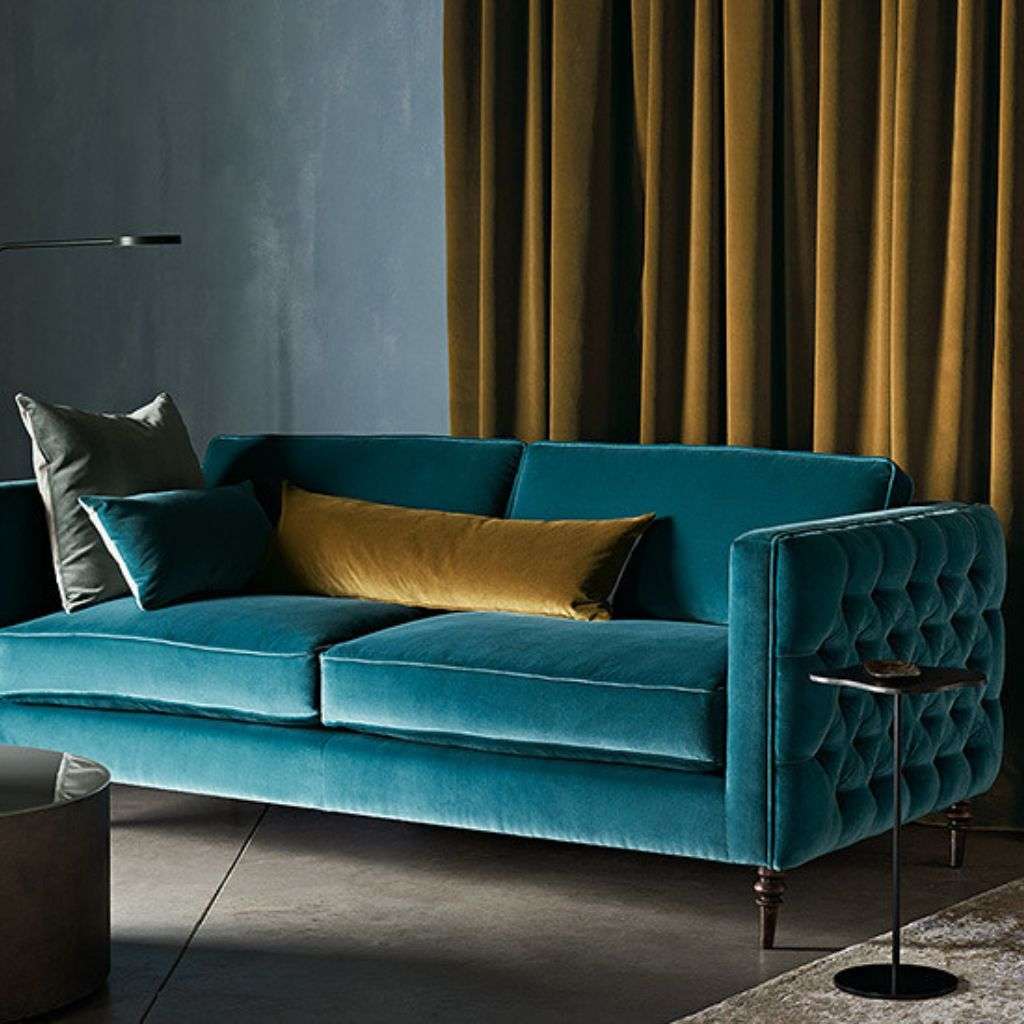 Romo deep blue velvet sofa with contrasting yellow pillows for luxurious comfort.