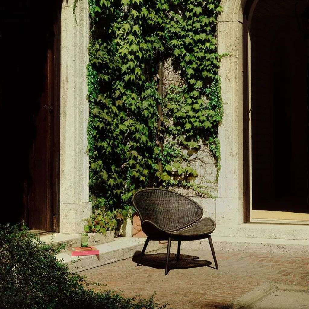 Single wicker lounge chair with lush greenery by Unopiu.