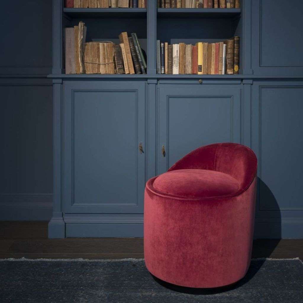 Villevenete velvet red chair in front of a blue library, exuding style and comfort.