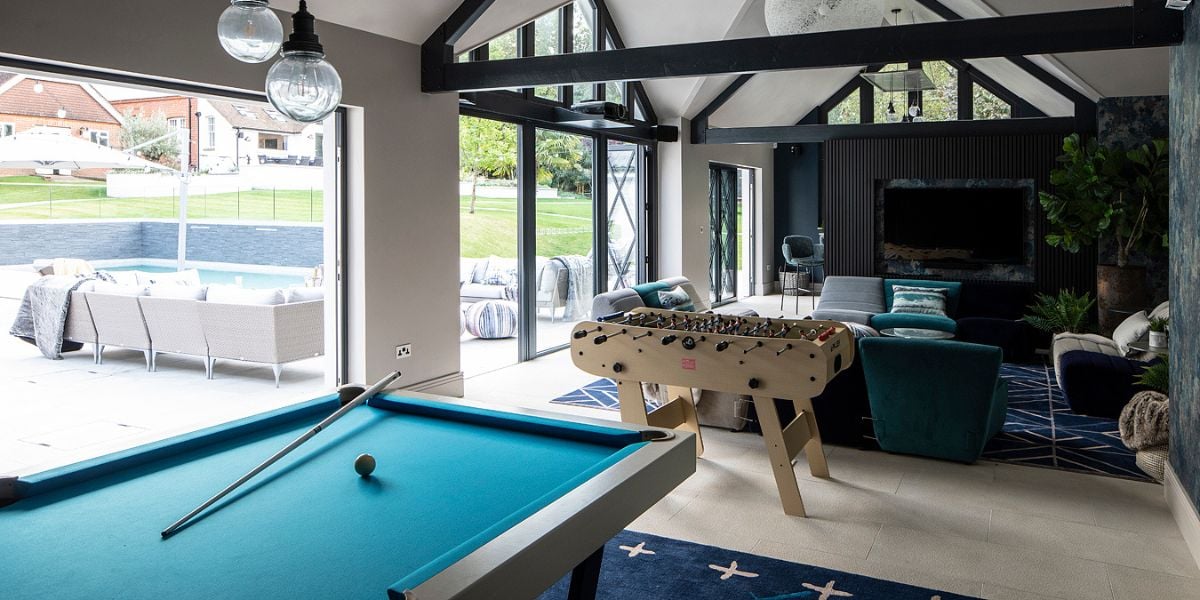 Open plan leisure and games room with pool table, foosball table, vaulted ceiling with exposed black beams, bifold doors opening to garden and pool beyond