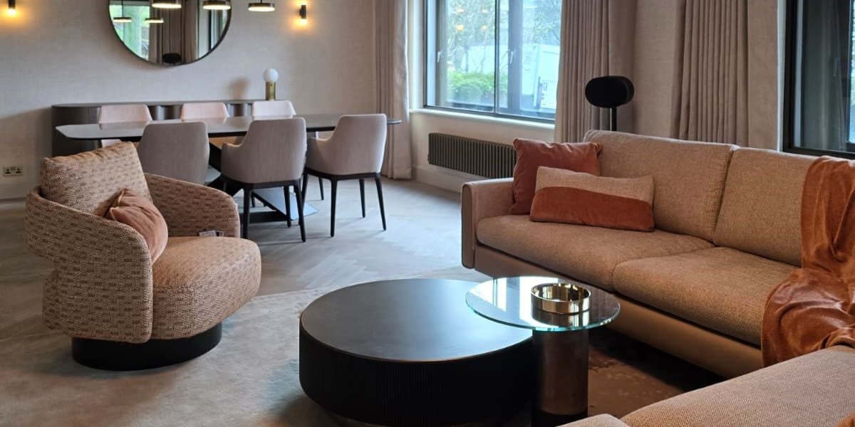 Warm open plan living and dining room with curved armchair, round low coffee tables, textured neutral sofa, orange cushions and dining table with dark chairs beyond