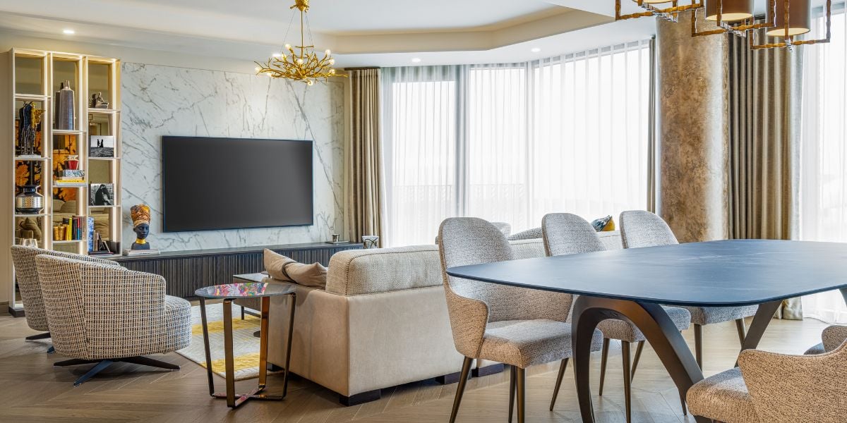 Open plan living and dining room with Calacatta marble TV feature wall, blue oval dining table, herringbone timber floor, brass-toned chandelier and backlit display shelving