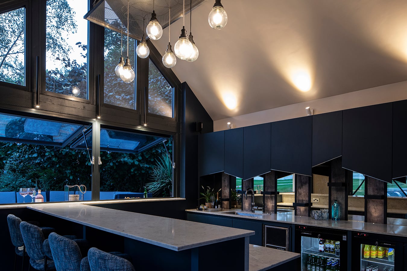 Navy blue kitchen wall at night with pendant lighting and bar stools